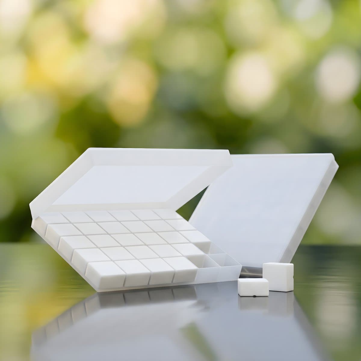 White troche tablet tray with individual square dose wells, soft green bokeh background